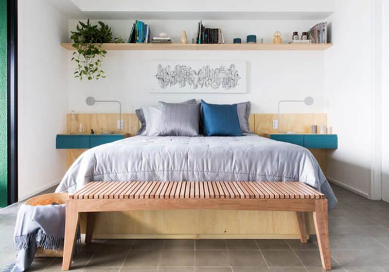 Quarto mobiliado com cama de casal, recamier, cabeceira de madeira e nichos com plantas.