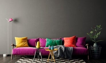 Sala com sofá roxo, almofadas coloridas e tapete com padrão preto e branco.