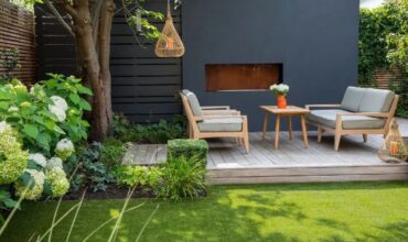 jardim-área-externa-com-um-deck-dois-sofás-mesa-de-centro-com-jarro-de-flores