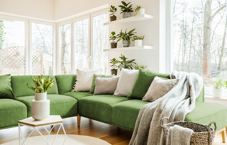 sofá de canto na cor verde com almofadas manta e grandes janelas ao fundo istock 